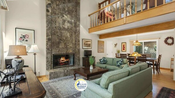 Ein geräumiges Wohnzimmer mit Kamin, einem grünen Sofa, einem Essbereich und einer Holztreppe.