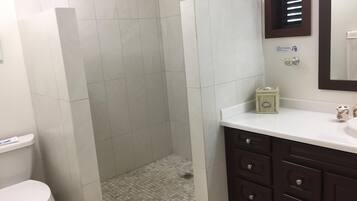 Een badkamer met douche, toilet en een wastafel met lades.