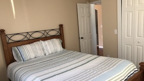 Une chambre à coucher avec une tête de lit en bois, une couvre-lit à rayures et une porte blanche en arrière-plan.