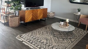 Ein modernes Wohnzimmer mit Flachbildfernseher, Holzschrank, Deckenventilator und einem gemusterten Teppich.