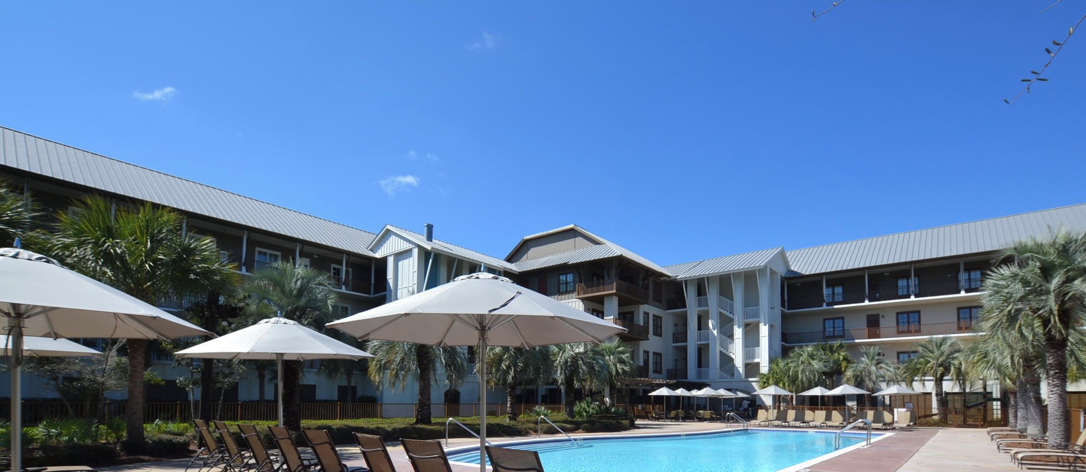 A hotel with a swimming pool, sun umbrellas, and palm trees.