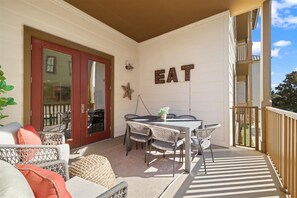 A covered outdoor patio with a dining table and chairs, a red door, and a wall-mounted sign that reads "EAT". - 2 BR/2.5 BA condo/Redfish Village/Pool/Walk to beach/Beach chairs/umbrella (Santa Rosa Beach)