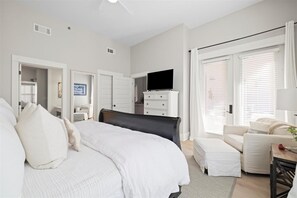 A bedroom with a large bed, a TV on a dresser, a sofa, and a window with blinds. - 2 BR/2.5 BA condo/Redfish Village/Pool/Walk to beach/Beach chairs/umbrella (Santa Rosa Beach)