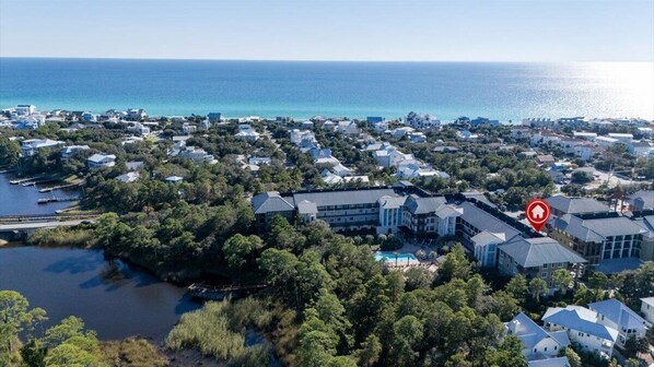 An aerial view of a coastal residential area with houses, a large building with a swimming pool, and a body of water. - 2 BR/2.5 BA condo/Redfish Village/Pool/Walk to beach/Beach chairs/umbrella (Santa Rosa Beach)