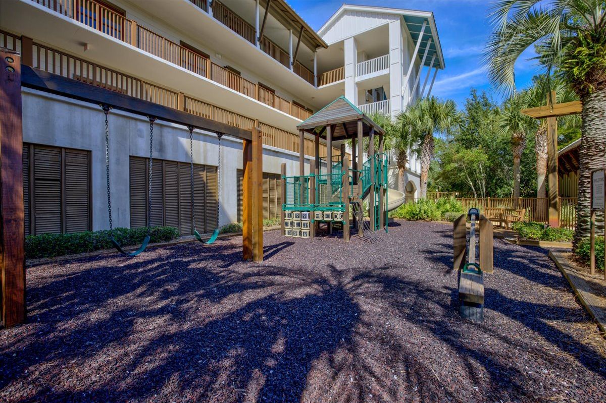 Un patio de hotel con un parque infantil, palmeras y una zona de estar cubierta.