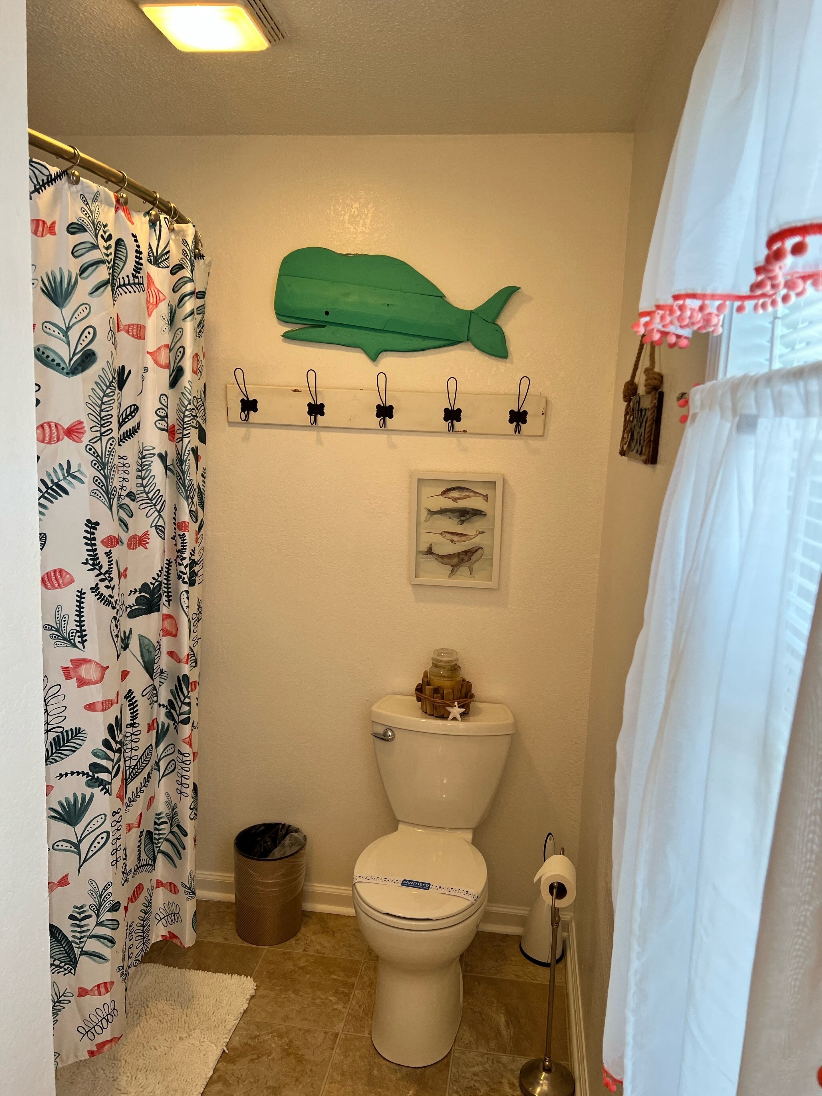 Ein Badezimmer mit Toilette, einer Wanddekoration mit Fischen, einem Hakenregal und einem Mülleimer.