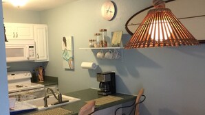 A kitchen with a microwave, sink, and bar area with two chairs. - Milepost 9 KDH Condo Oceanside (Kill Devil Hills)