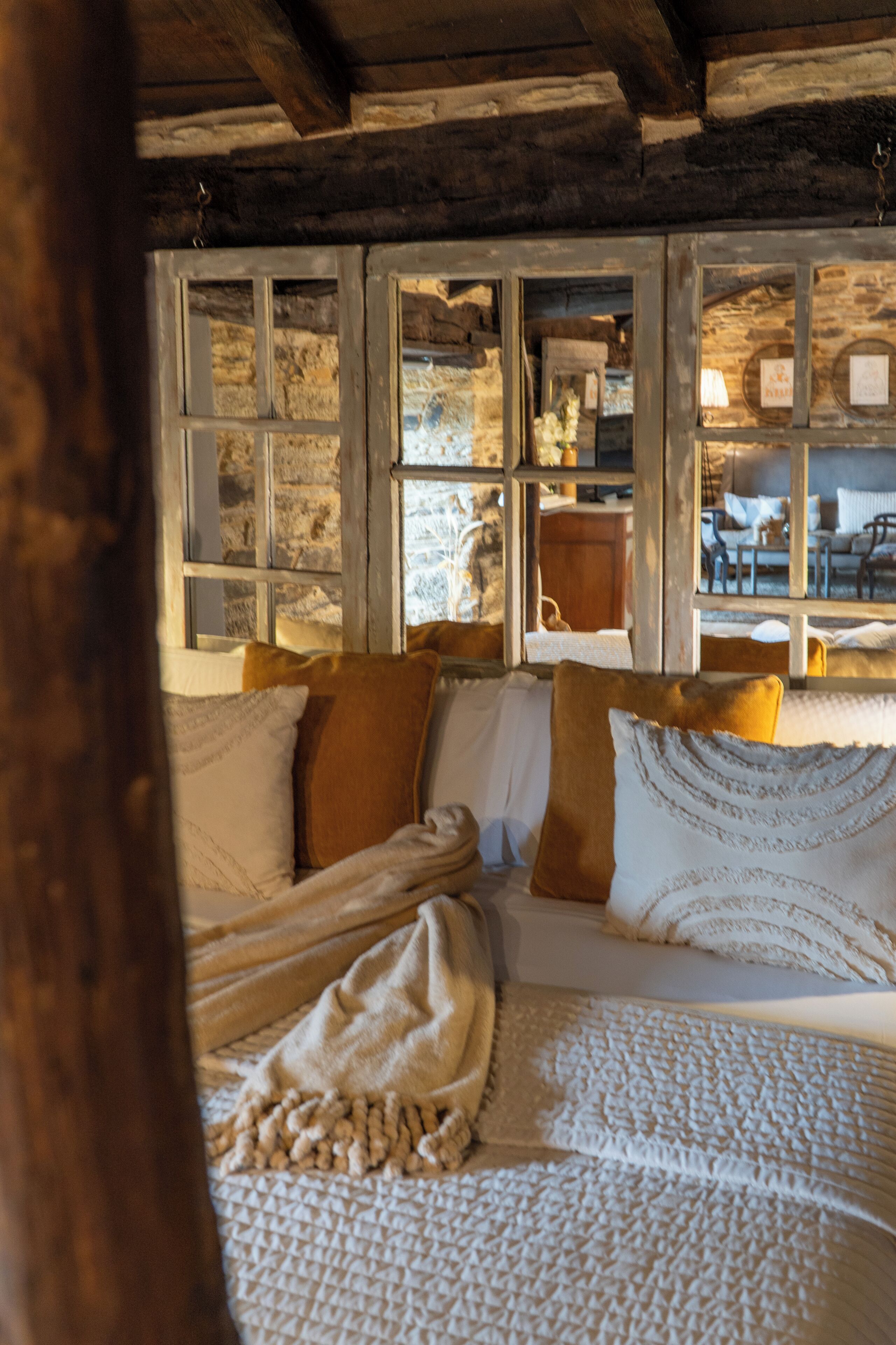 Une pièce rustique avec un plafond en bois, un lit recouvert d’une courtepointe à motifs et un mur en pierre avec une fenêtre.