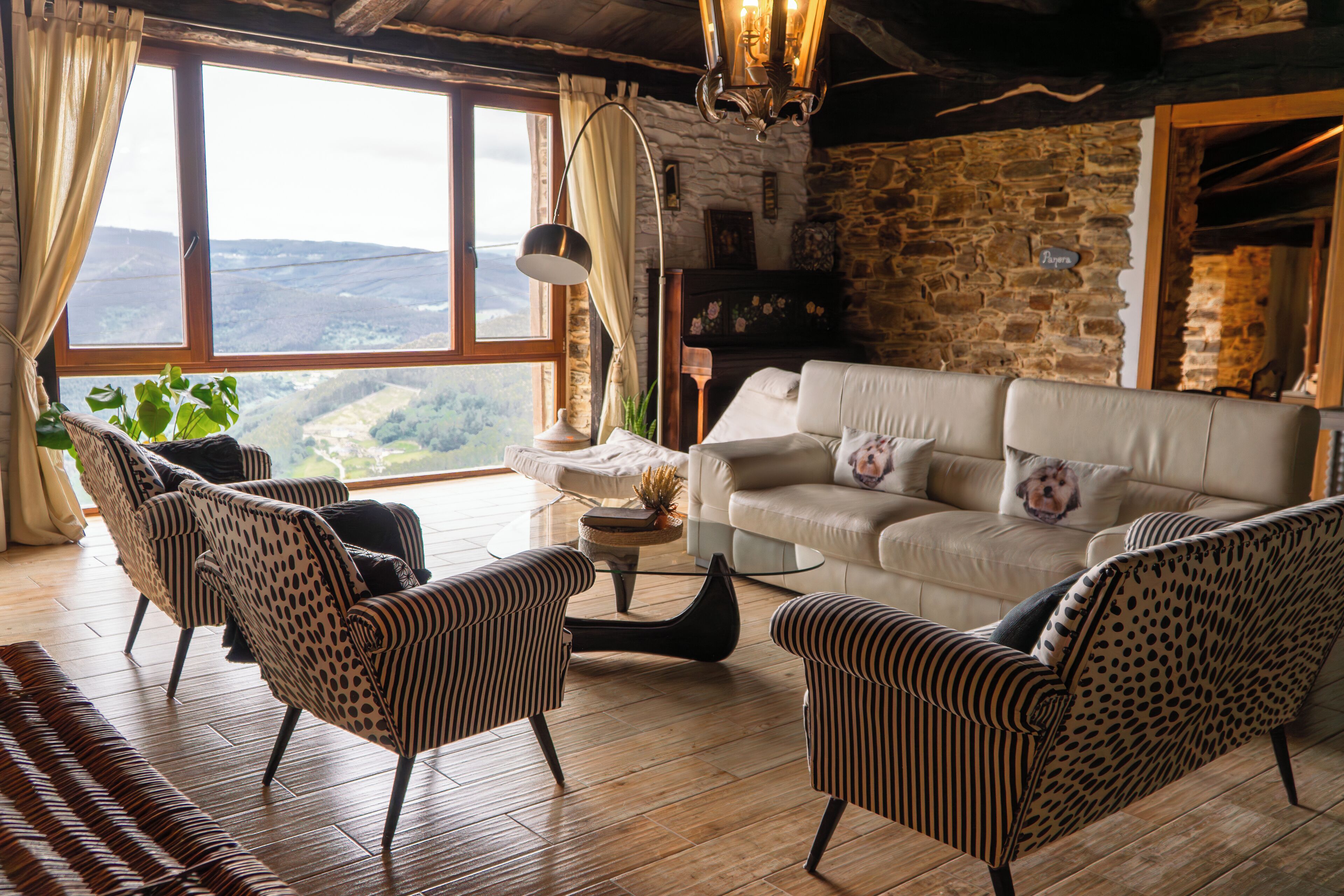 A cozy living room with a stone wall, a large window with a view, and striped armchairs.