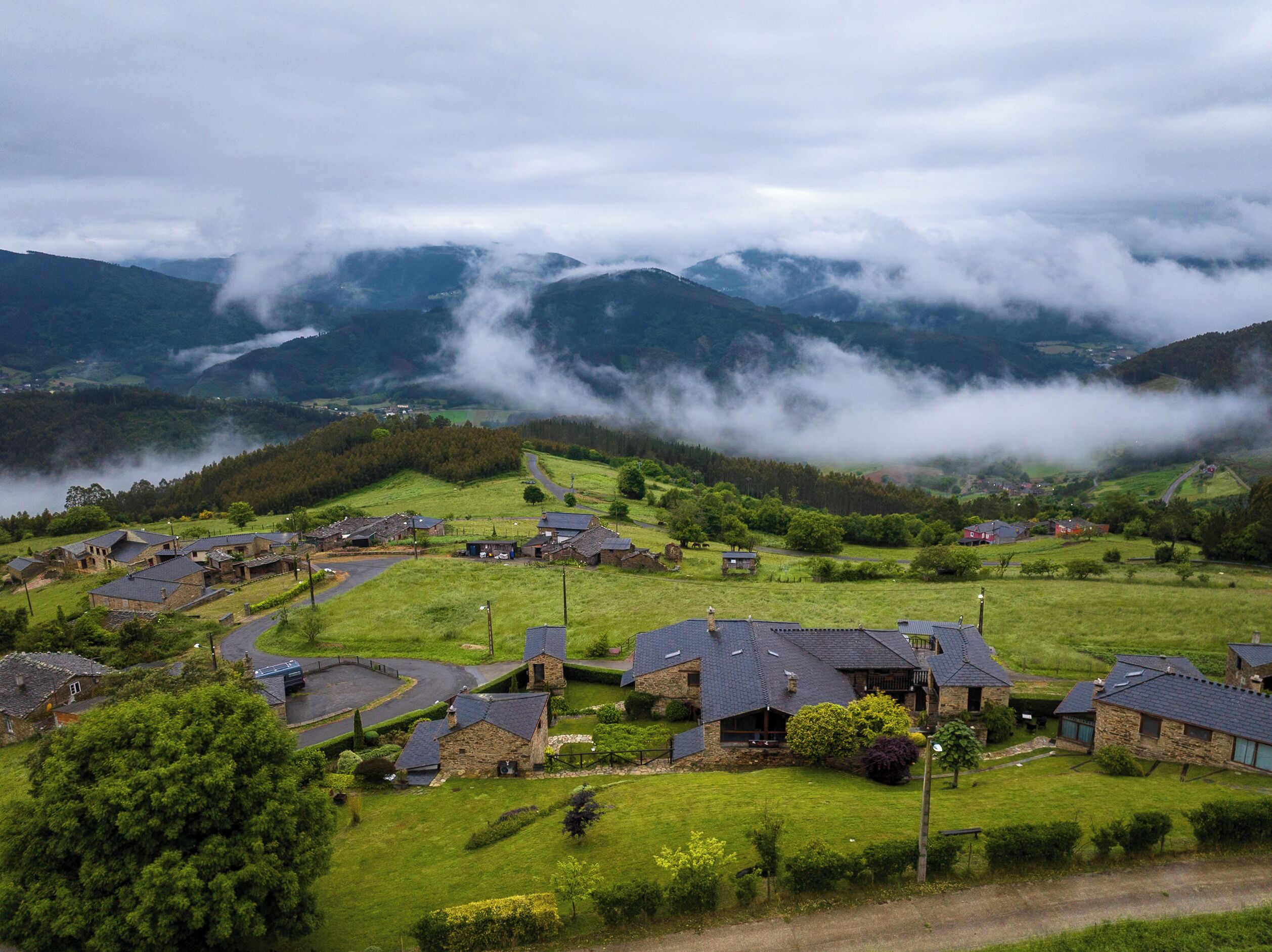 A rural village with stone houses, winding roads, and a valley surrounded by mountains.