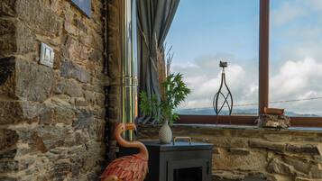 Un interior rústico con una pared de piedra, una chimenea y vistas a través de una ventana.