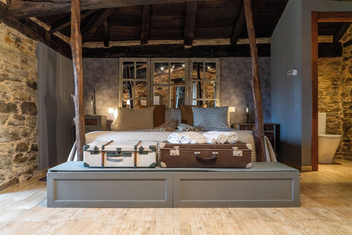 A bed with a headboard, a stone wall, and a wooden ceiling.