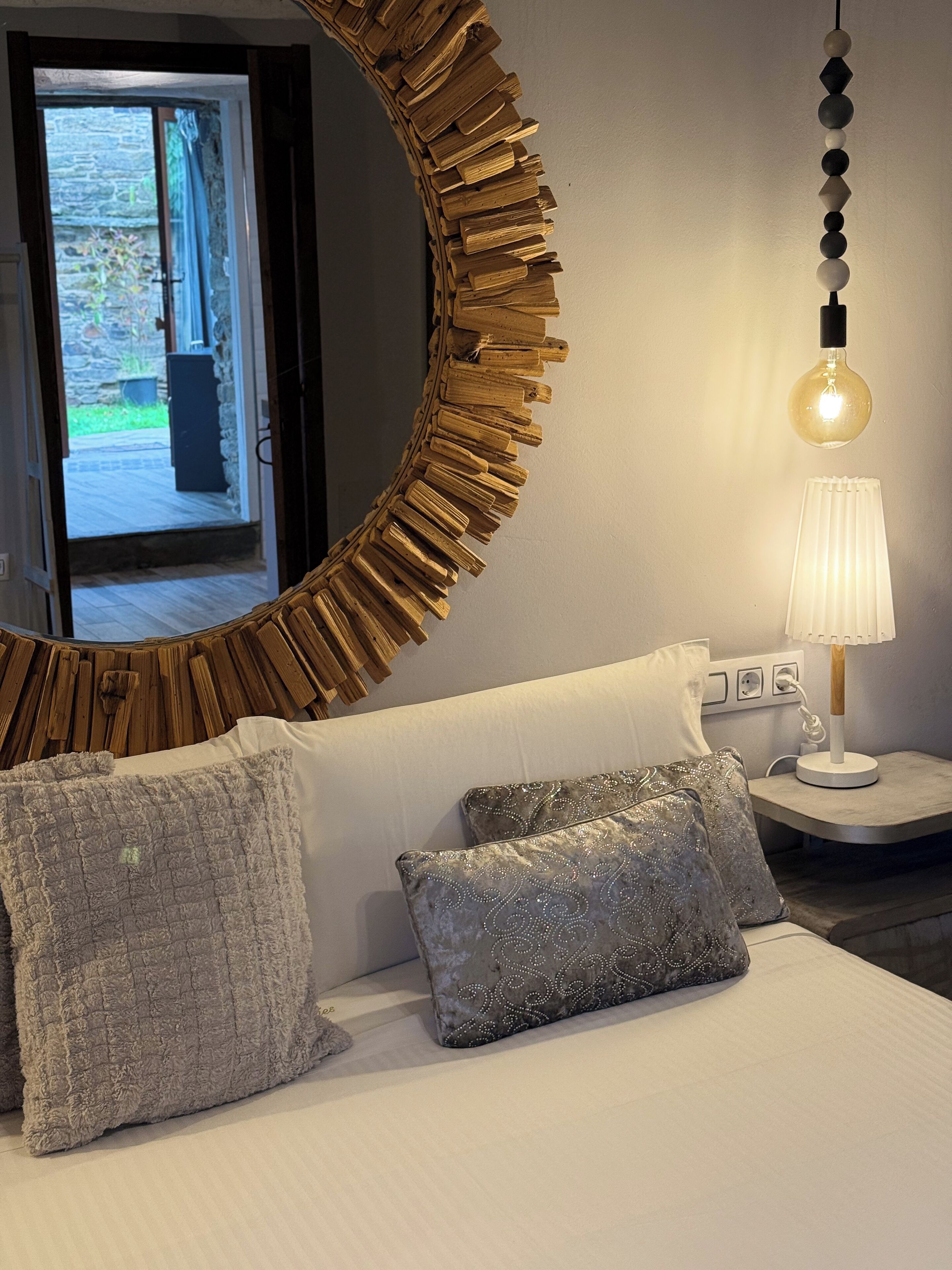 A bedroom with a large mirror, a bedside table with a lamp, and two decorative pillows.