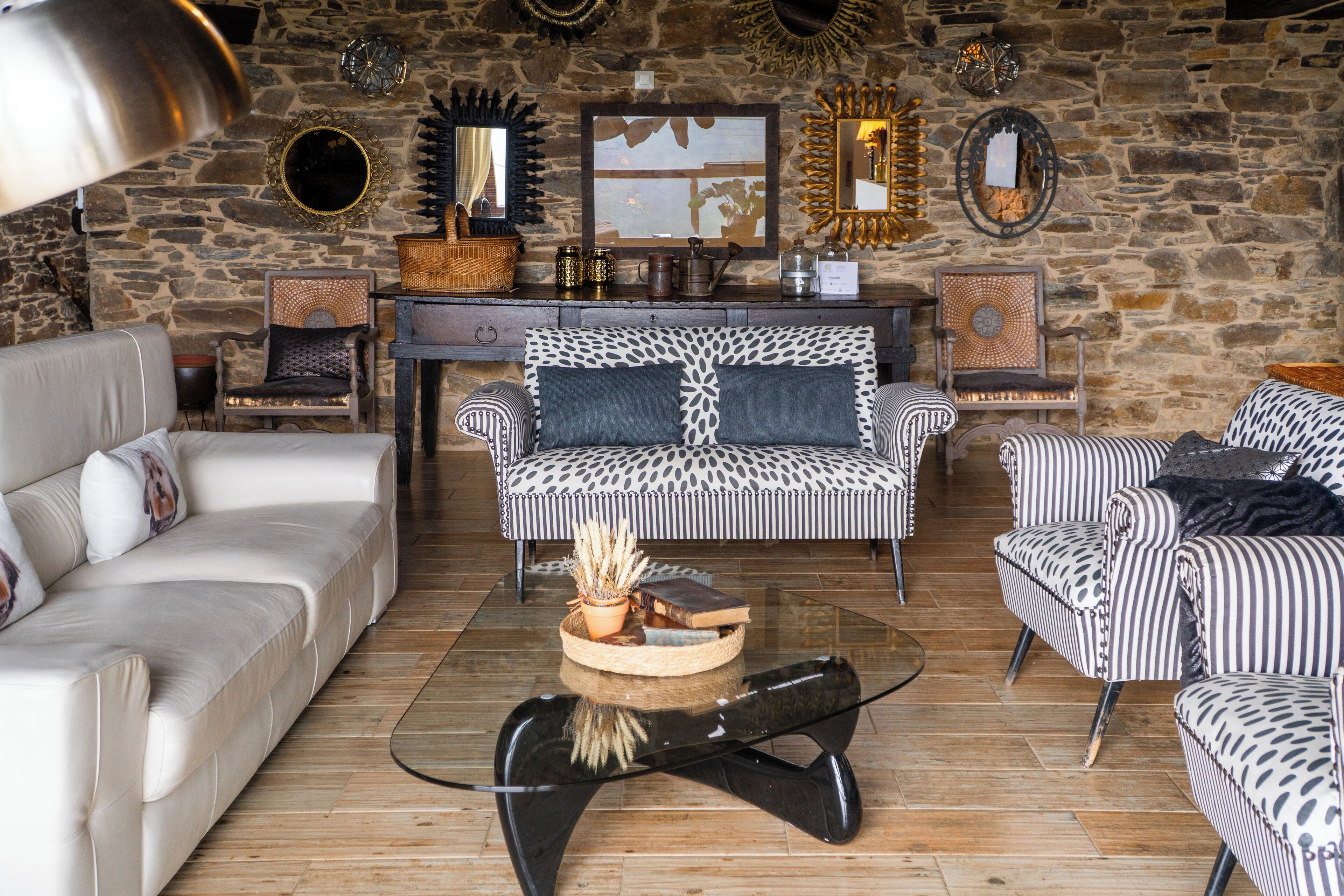 A cozy living room with a stone wall, a white sofa, a patterned armchair, and a glass coffee table.