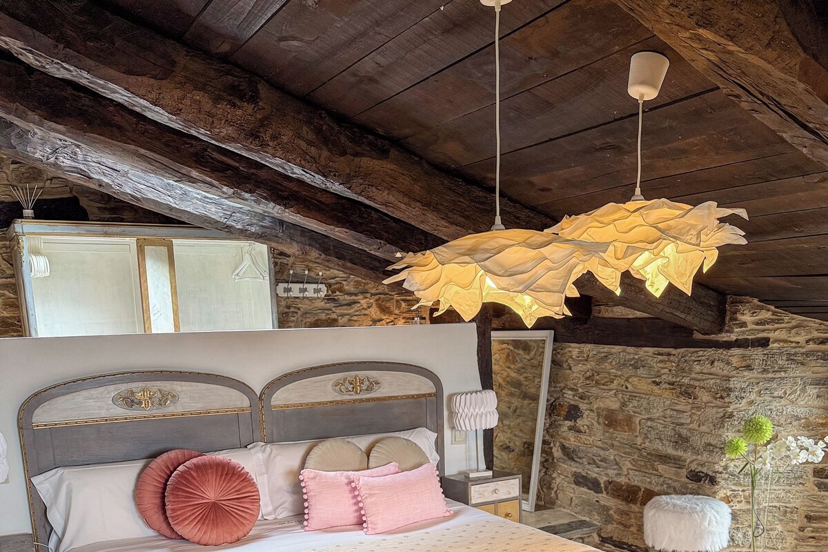 A bedroom with a large bed, a wooden ceiling, and a rustic stone wall.