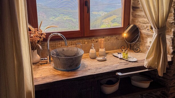 A rustic kitchen with a large window, wooden counter, and stone wall. - Complejo Rural Lar de Vies (A Pontenova)