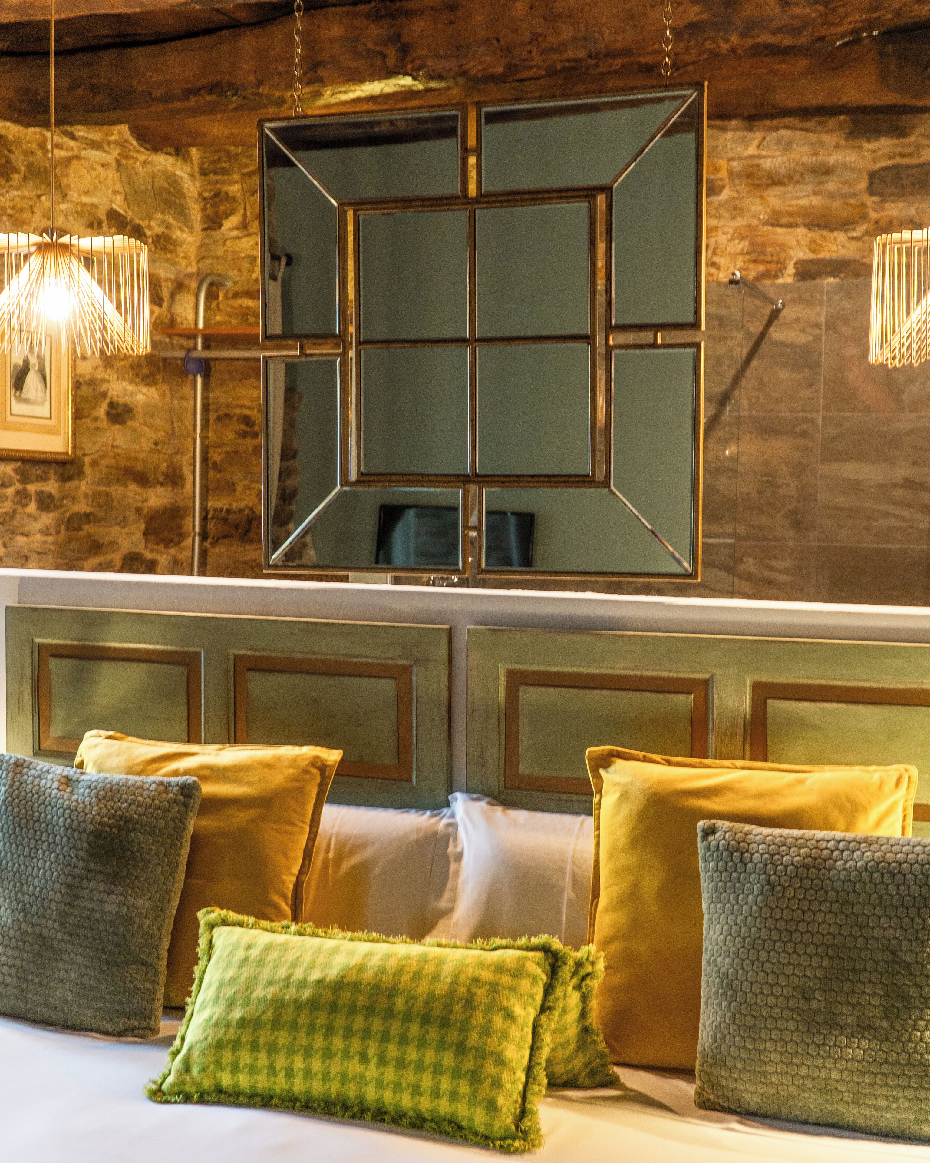 A hotel room with a stone wall, a large mirror, and a bed with multiple pillows.