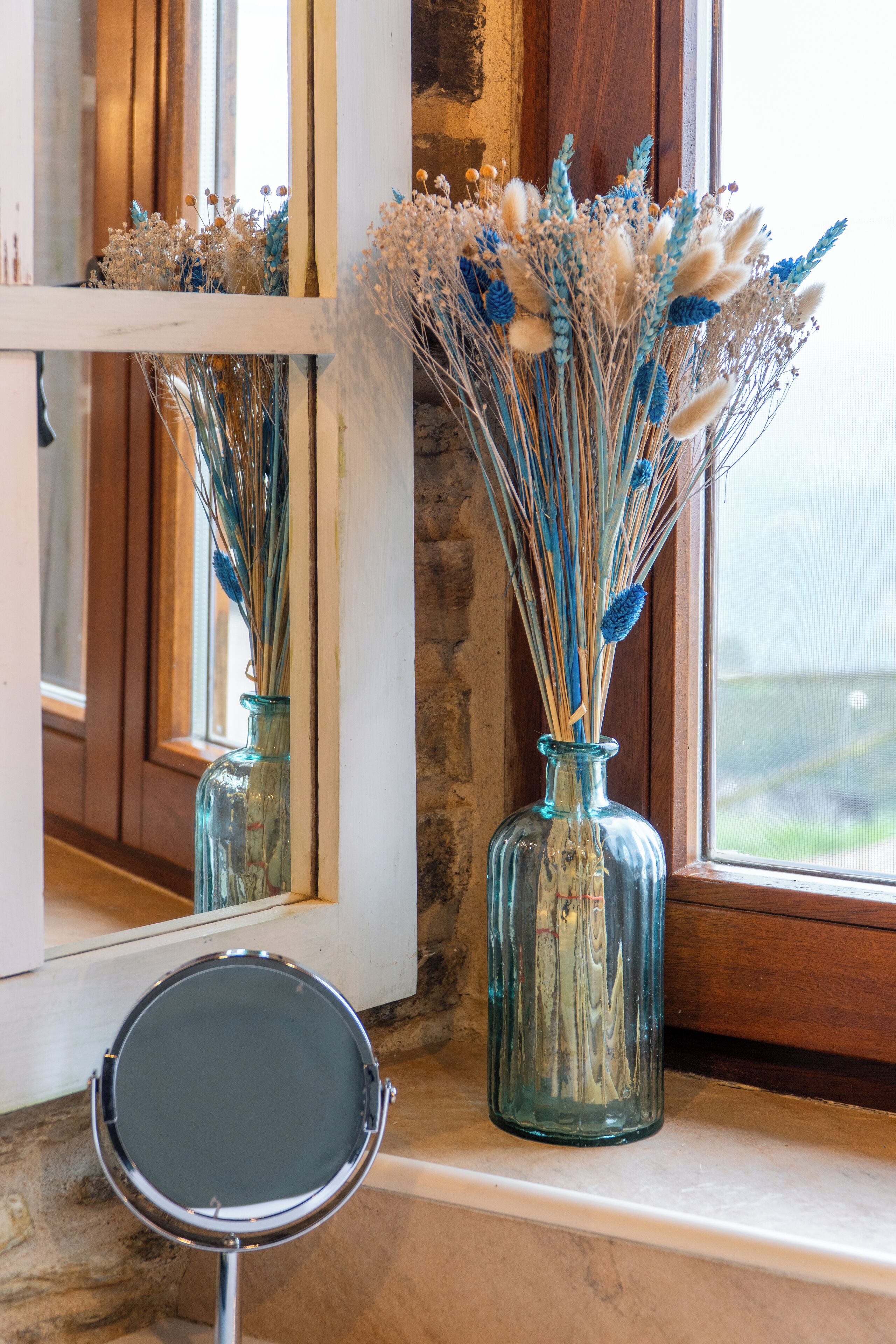 Two glass vases with dried flowers on a windowsill.