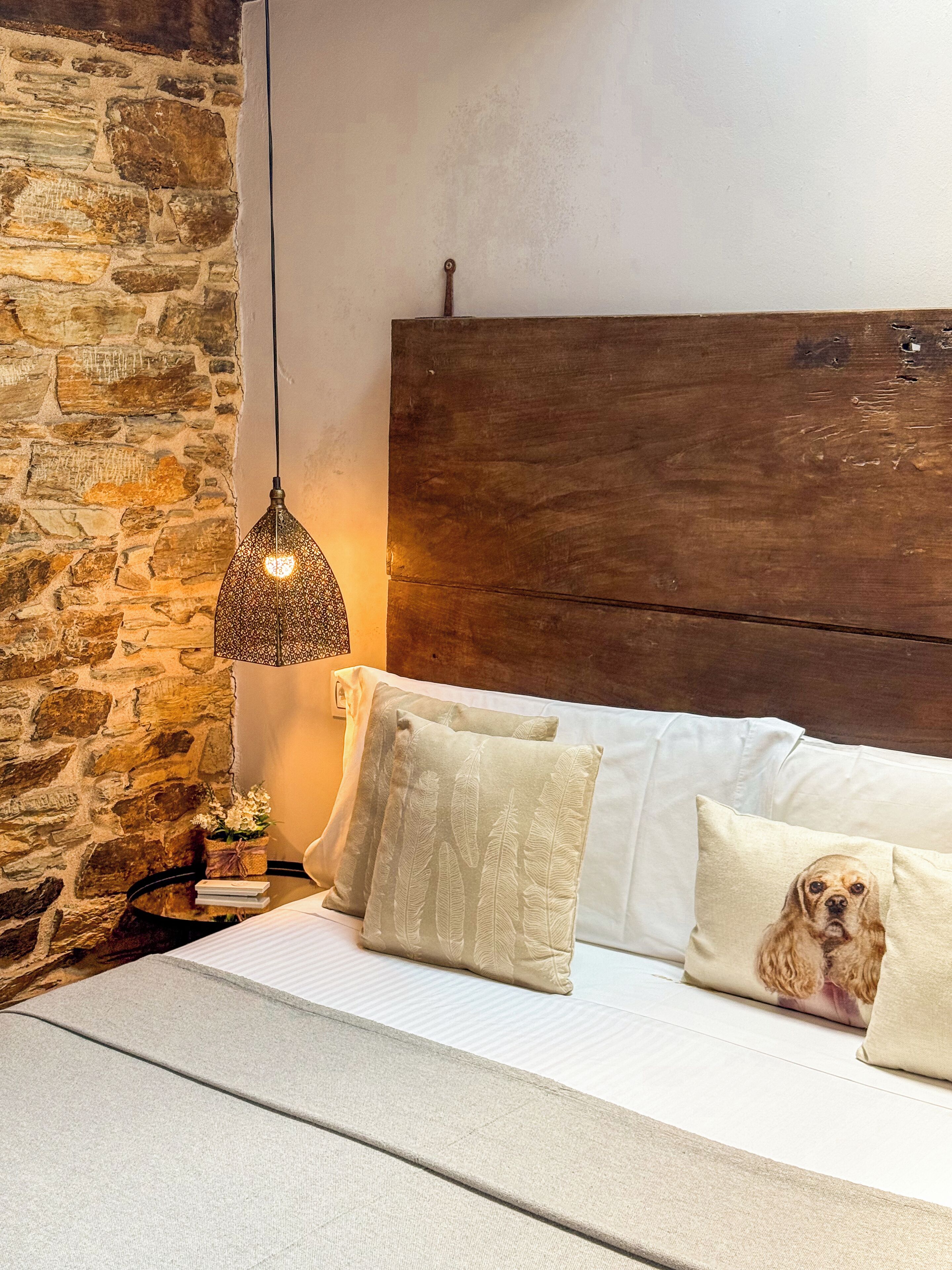 Un dormitorio con pared de piedra, cabecera de madera y lámpara colgante.