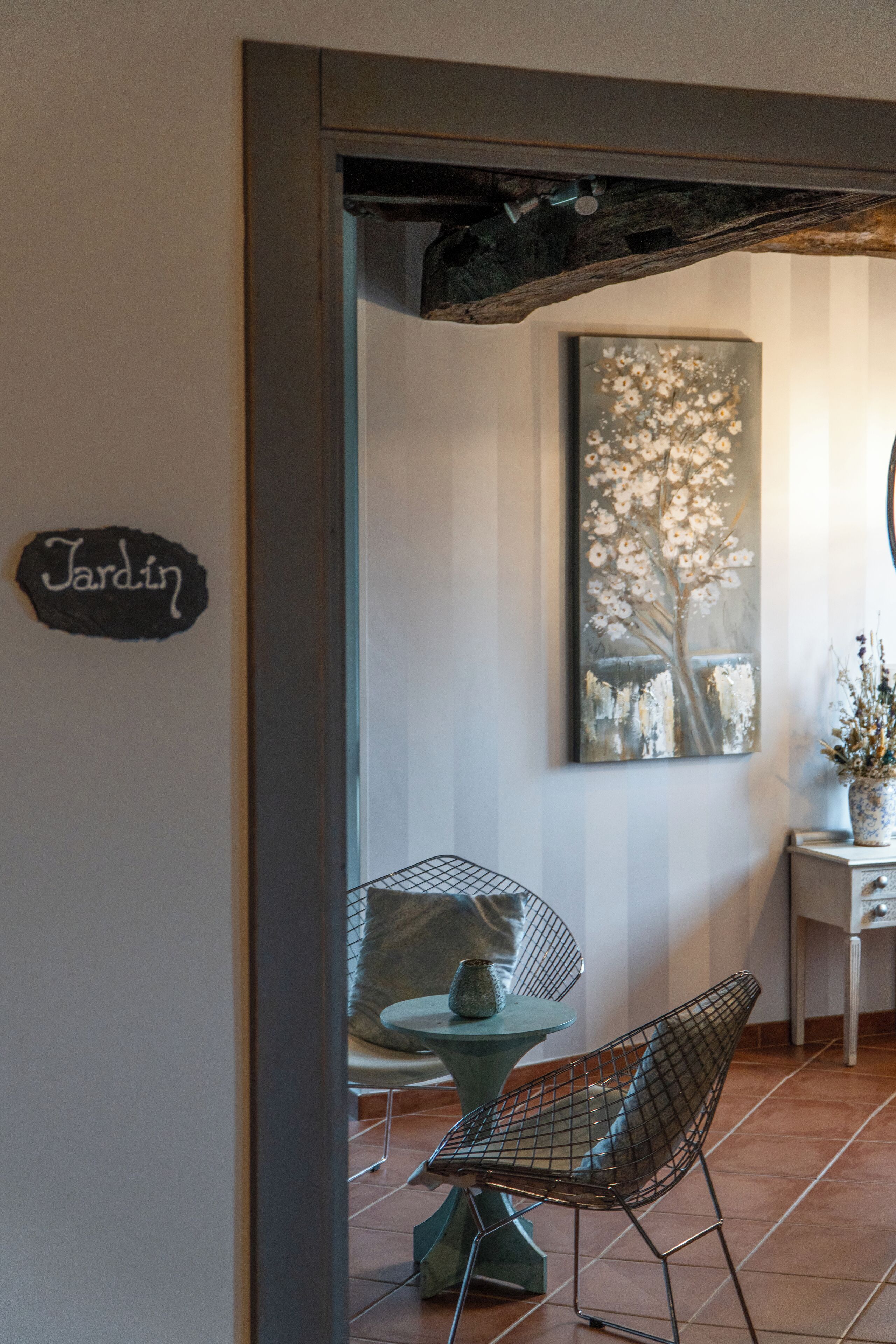 Een eethoek met een tafel en stoelen, een bord met de tekst 'Jardin' en een bloemen schilderij aan de muur.
