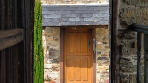 A stone building with a wooden door, a stone staircase leading to the door, and a small potted plant beside the door. - Complejo Rural Lar de Vies (A Pontenova)