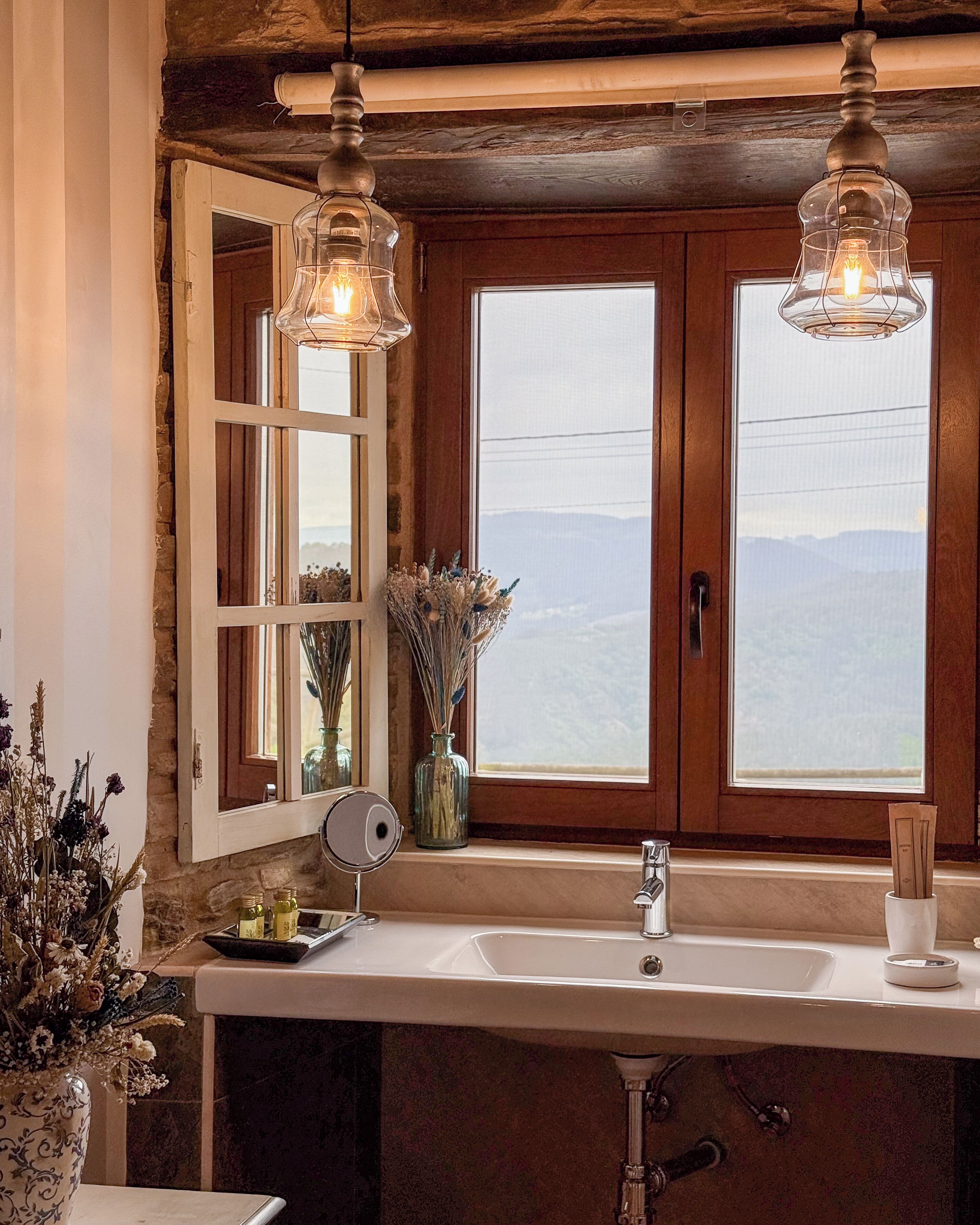 A bathroom with a large window, a sink, and two pendant lights.