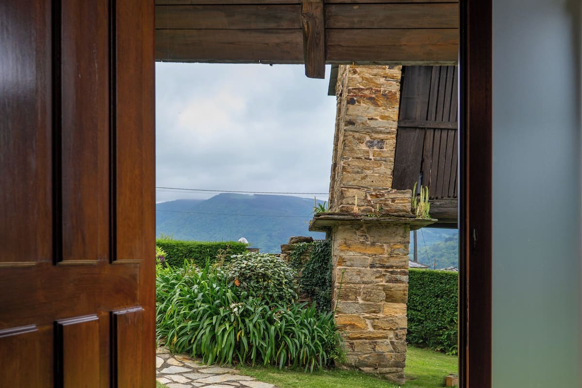 A stone pathway leading outside a wooden door, with a stone pillar and a view of the outdoors.