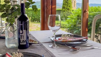 Una mesa dispuesta con una botella de vino, una copa, platos y cubiertos, con una vista panorámica a través de la ventana.