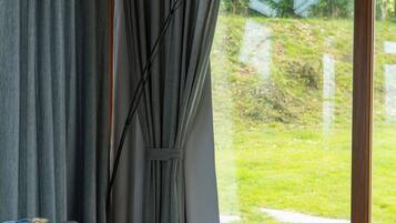 A room with a grey sofa, a leopard print pillow, grey curtains, and a window with a view of a green lawn.