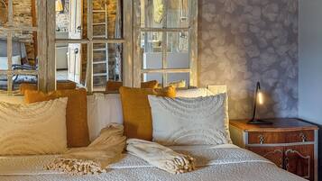 A cozy bedroom with a large bed, wooden beams, stone walls, and a view through a window.
