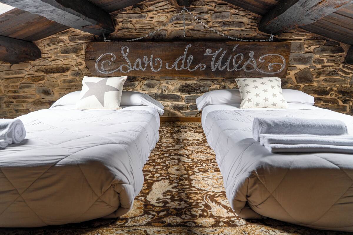 A rustic stone-walled room with two beds, each with a star-patterned pillow and a rolled towel.