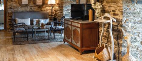 A rustic stone-walled living room with a sofa, chairs, a television, and a relaxation area with towels.