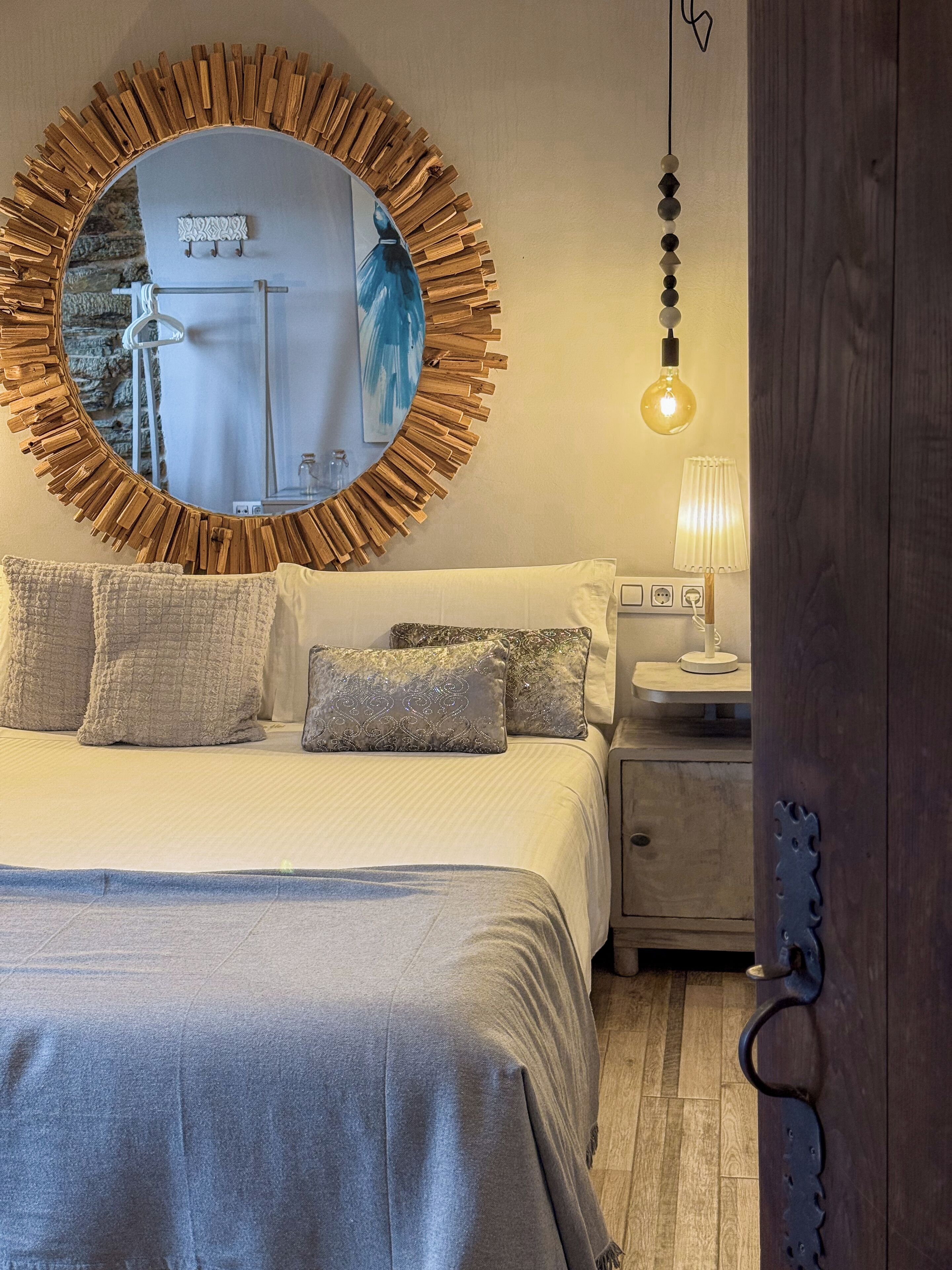 A bedroom with a large circular mirror, a bedside table with a lamp, and a bed with multiple pillows.