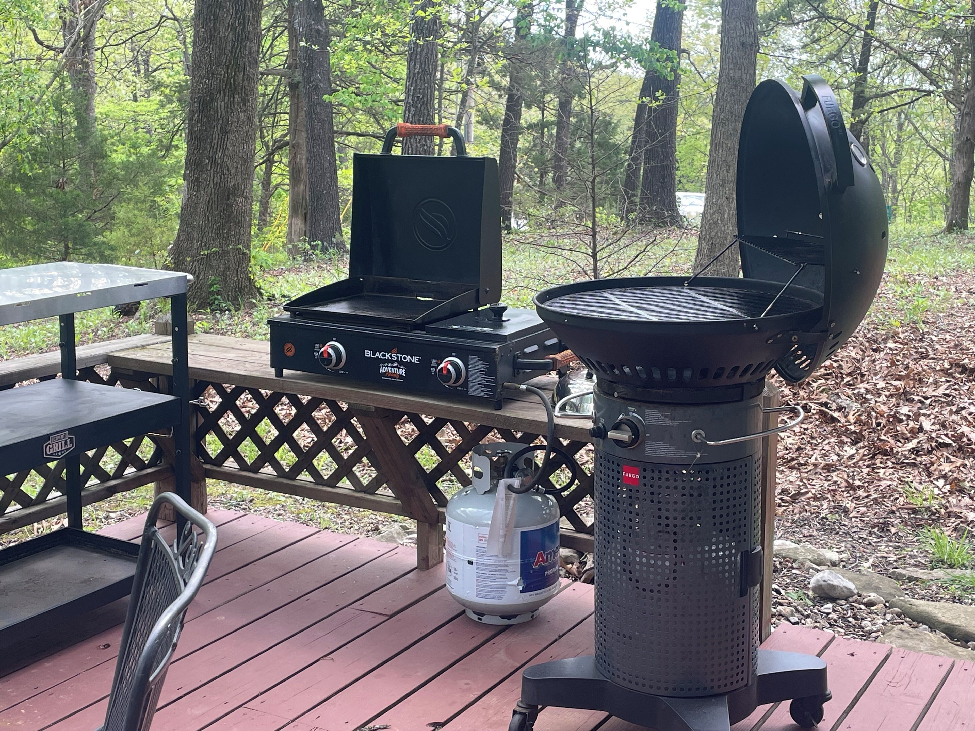 Ein Grillplatz mit Grill, einem tragbaren Gasherd und einer Propangasflasche auf einer Holzterrasse.