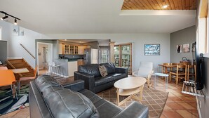 A spacious living room with a black leather sofa, a wooden dining table, and a kitchen in the background. - Lakefront 3-BR Home Summer Getaways & Sports Force (Sandusky)