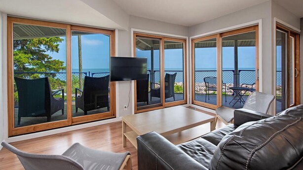 A modern living room with a large TV, comfortable seating, and a balcony with a view of the sea. - Lakefront 3-BR Home Summer Getaways & Sports Force (Sandusky)