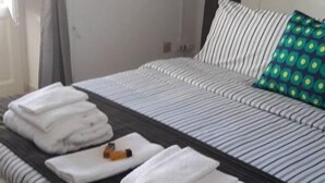 A neatly made bed with striped bedding, a green patterned pillow, and folded white towels on a dark headboard. - B&B Dietro al Massimo (Palermo)
