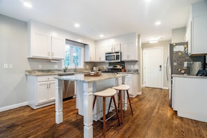A modern kitchen with white cabinetry, a central island with stools, a microwave, and a refrigerator.