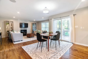 A spacious living room with a fireplace, a dining area with a table and chairs, and a large sliding glass door leading to a balcony.