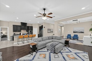 A modern living room with a sectional sofa, a dining area with bar stools, and a kitchen with dark cabinets.
