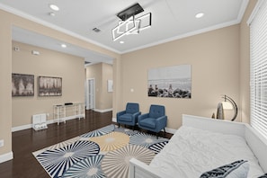 Une chambre d’hôtel moderne avec un grand lit, deux fauteuils bleus, un tapis à motifs et des œuvres d’art accrochées aux murs.