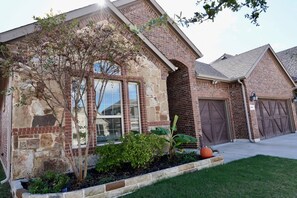 A brick house with a stone facade, a garage, and a well-maintained garden with a pumpkin.