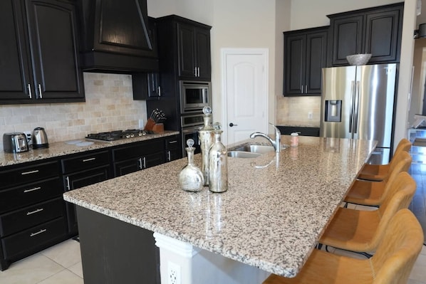 A kitchen with dark cabinets, a granite countertop, stainless steel appliances, and a large island with bar stools.