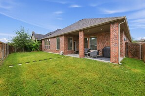 Une maison d’habitation dotée d’un patio couvert, d’une façade en briques et d’une pelouse bien entretenue.