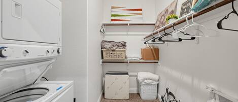 Une buanderie équipée d’un lave-linge, d’un étendoir et d’étagères où sont pliés les vêtements.