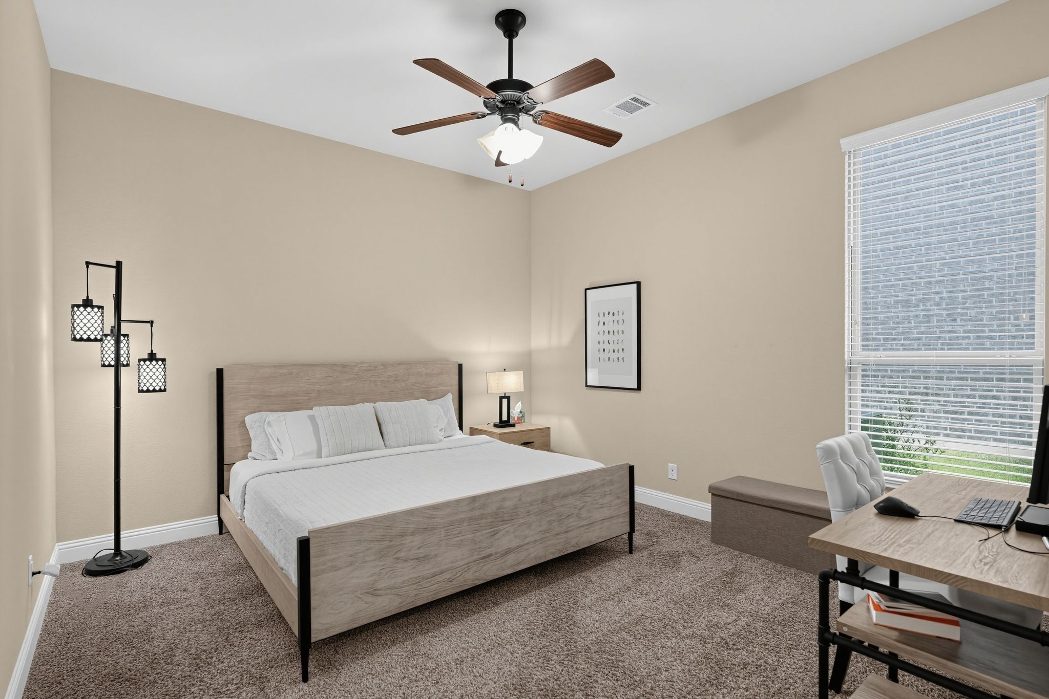 A bedroom with a bed, a desk with a computer, a ceiling fan, and a window with blinds.