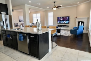 A modern kitchen with a central island, dark cabinetry, and a dining area with blue chairs.