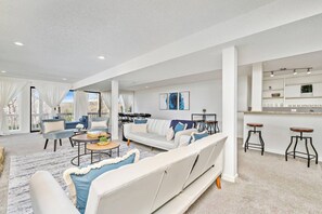 A spacious living area with a sofa, chairs, and a coffee table. There is a kitchen area with stools and a counter.