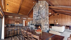 A rustic interior with a stone fireplace, wooden dining table, and bar stools. - Beautiful, large, private home in Fox Acres- huge patio w/ gorgeous views! (Red Feather Lakes)