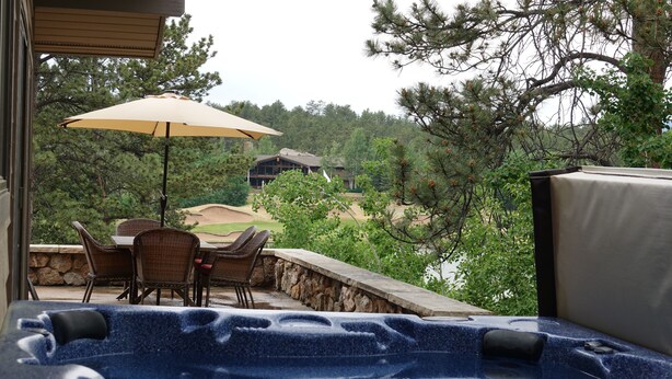 A hot tub with a stone wall and a dining area with chairs and an umbrella. - Beautiful, large, private home in Fox Acres- huge patio w/ gorgeous views! (Red Feather Lakes)